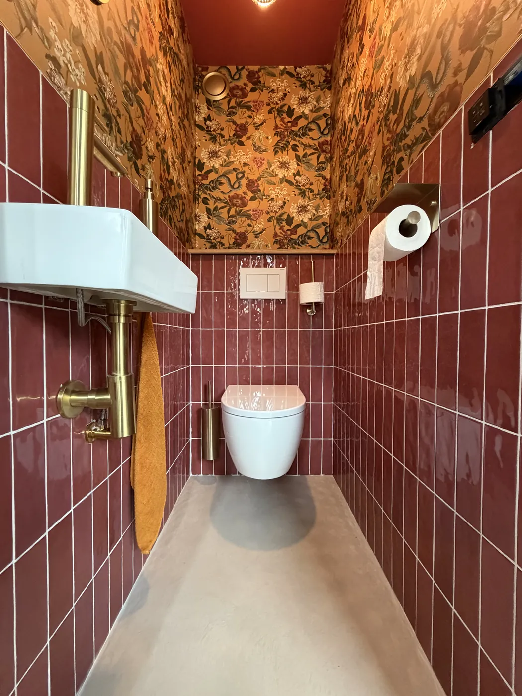 Gietvloer naast bordeauxrode wandtegels in het toilet